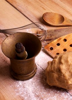 Arrangement of Dough, Wooden Kitchen Utensils, Old Bronze Mortar and Pestle with Flour on Wooden background