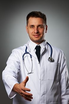 Medical doctor with stethoscope giving hand for handshaking against grey background 