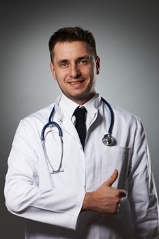 Medical doctor with thumb up portrait against grey background 