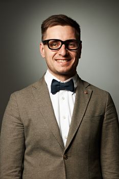 Confident nerd in eyeglasses and bow tie against grey background