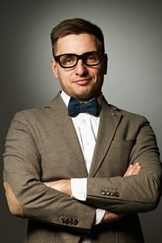 Confident nerd in eyeglasses and bow tie against grey background