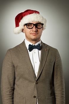 Confident nerd in Santa Claus hat and bow tie celebrates Christmas