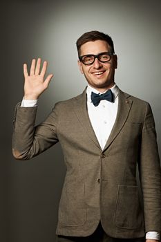 Nerd in eyeglasses and bow tie says Hello against grey background