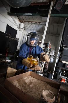 Young glass worker in protective suit and helmet with hot jar