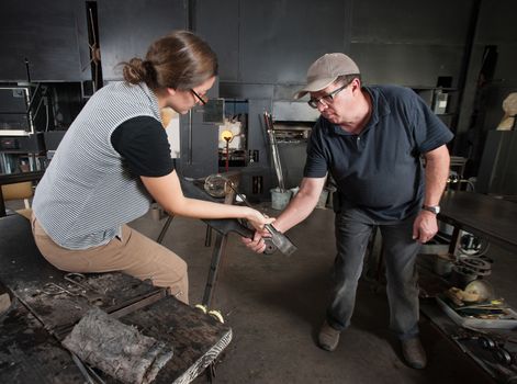 Glass artisan helping young student create glass vase