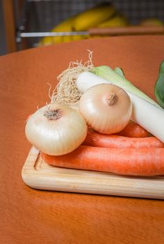 Fresh vegetables on cutting board in a wooden kitchen table