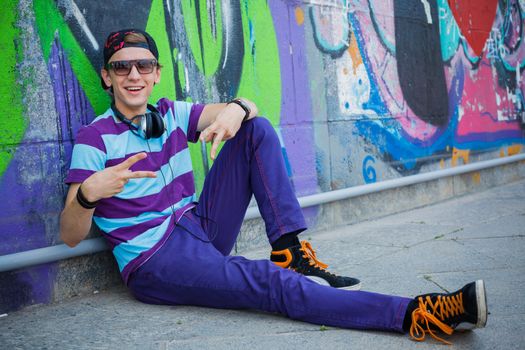 Happy teens boy with headphones near painted wall listening to music