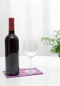 Bottle of red wine and glass on a white table.