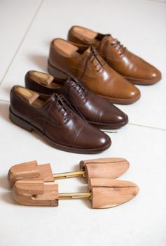 Two pairs of brown handmade classic men's shoes  with a shoe pads and stretchers inside and beside the shoes