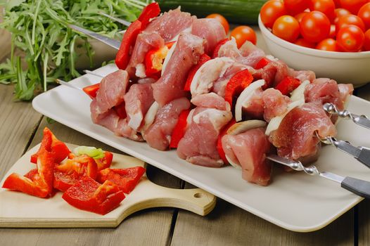 Raw shashlik - marinated meat for roasting on a skewers, with tomatoes, bell pepper and greenery.