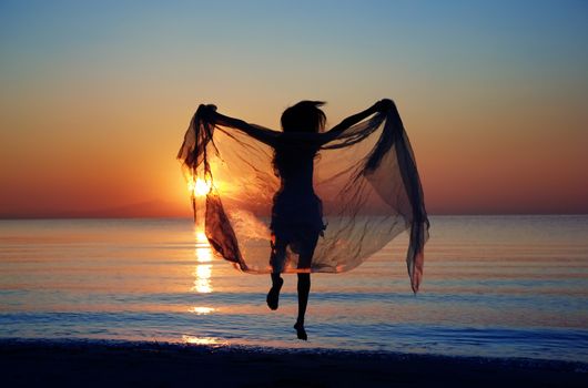 Rear view on the silhouette of the woman jumping at the beach during sunset. Natural darkness and colors