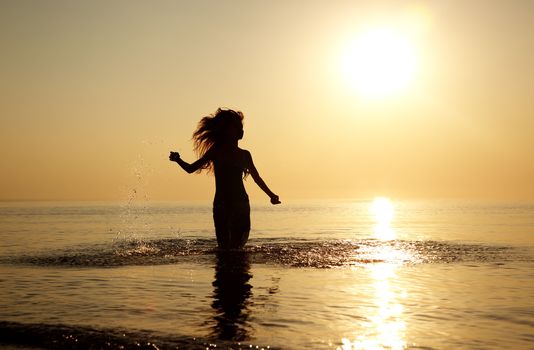 Silhouette of the woman with long hairs running at the beach during sunset. Natural light and colors