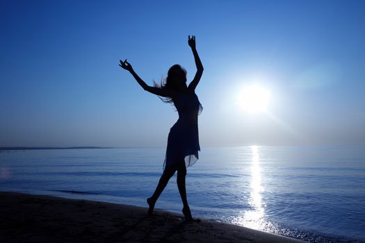 Silhouette of the woman with long hairs dancing at the beach during sunset. Artistic colors added