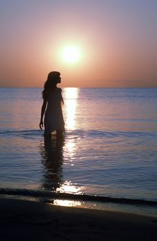 Silhouette of happy woman standing in the water at the beach during twilight