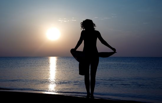 Silhouette of the woman standing at the beach during sunset