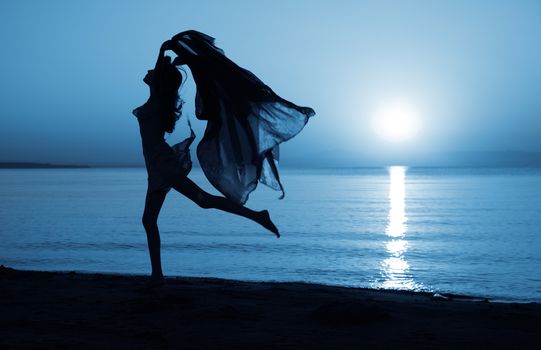 Silhouette of elegant lady dancing at the beach under the moonlight