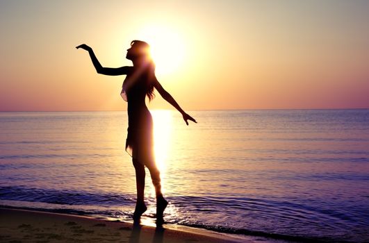 Silhouette of the woman dancing at the beach during beautiful sunrise. Natural light and darkness