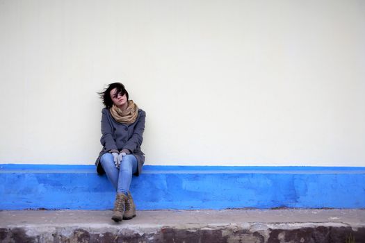 Beautiful young girl sitting against yellow wall