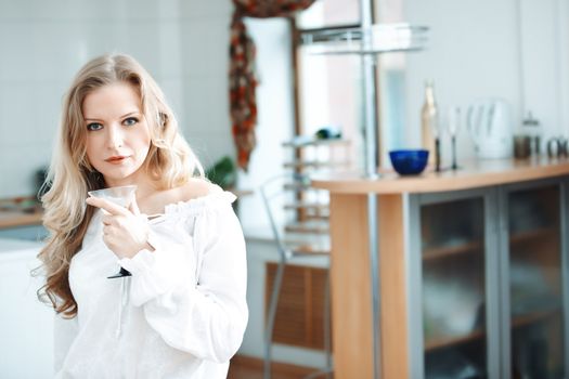 Blond lady holding wine glass with beverage at the kitchen