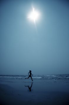 Woman at the beach running to the water in the deep dark night. Blue color toning added for coolness of the night