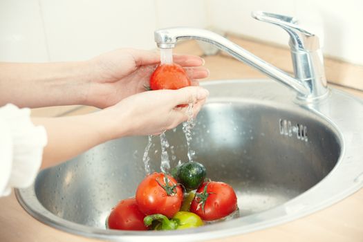 Hands of woman washing vegetables at her kitchen