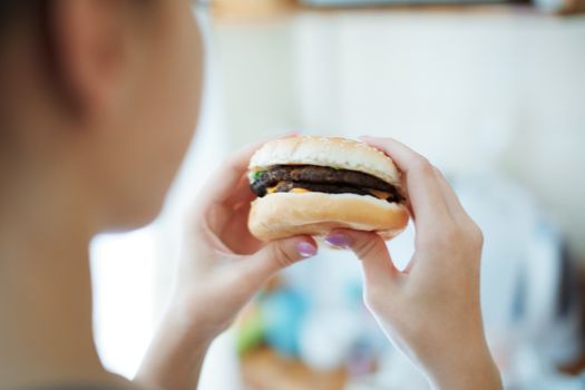 Woman eating hamburger. Rear view