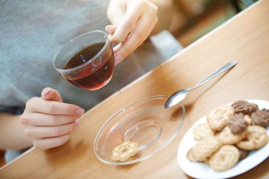 Woman hands holding cup of tea with cookie