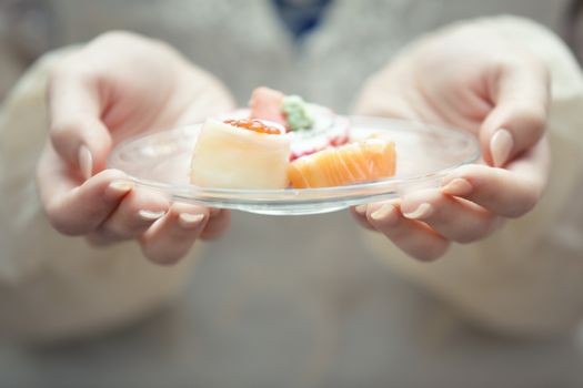 Human hands holding plate with sushi