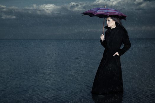 Lady with umbrella standing under the rain in the sea