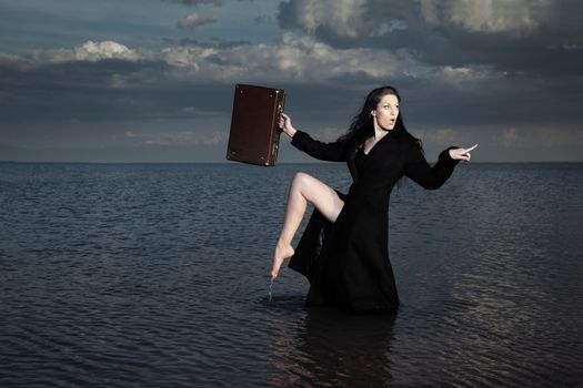 Stylish lady in the black coat with case standing in the dark water