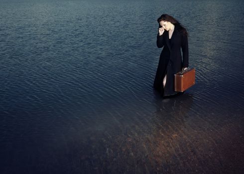Sad alone woman with bag standing in the water