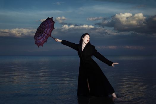 Businesswoman in the water with blown umbrella