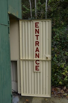 Corrugated metal workshop door with painted entrance sign in red.