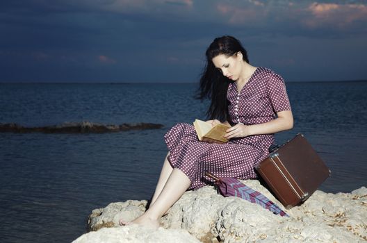 Single lady reading book outdoors at the ocean during sunset
