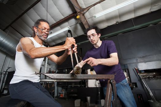 Assistant helping glass manufacturing worker with pliers