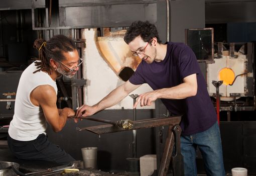 Two glass artisans working together on small vase