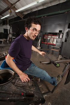 Serious young adult with tools and workbench in glass factory