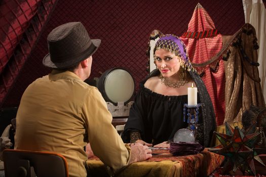 Smiling beautiful fortune teller with crystal ball and customer