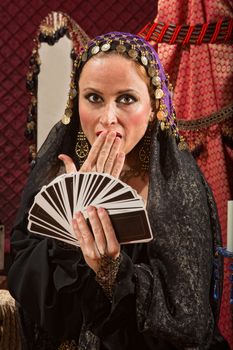 Surprised gypsy fortune teller with hand of tarot cards