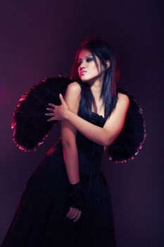 Brunette lady with black wings on a dark background. Colorful light added by the lighting filter in studio
