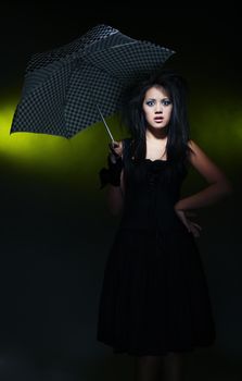 Brunette lady holding umbrella on a dark background. Artistic darkness and colors added