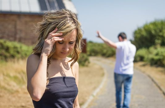 Unhappy frustrated woman in focus and angry man leaving on the background after quarrel