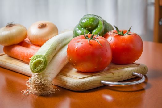 Fresh vegetables on cutting board in a wooden kitchen table