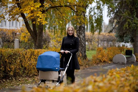 Mother with baby stroller for a newborn in autumn park