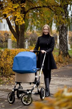 Mother with baby stroller for a newborn in autumn park