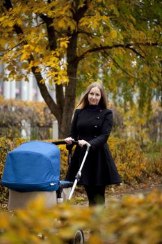 Mother with baby stroller for a newborn in autumn park