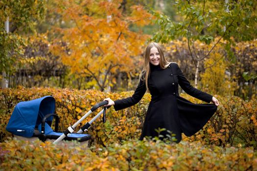 Mother with baby stroller for a newborn in autumn park