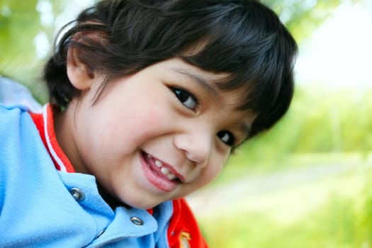 Happy toddler boy smiling, looking sideways at camera, outdoors with sun rays