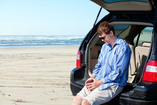 Caucasian man in car at beach, looking down unhappy, worried expression