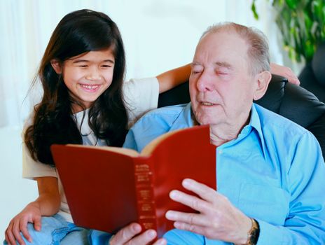 Elderly man and little girl reading Bible together, great grandpa and great granddaughter.